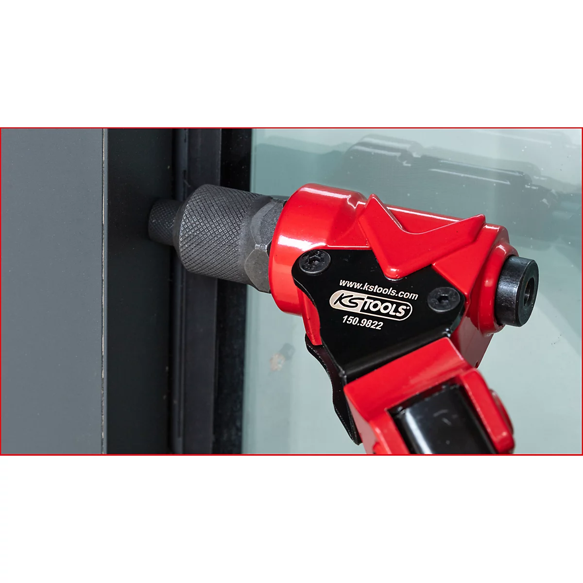 Ein rotes KS Tools-Werkzeug im Einsatz beim Einsetzen eines Metallbolzens in einen Fensterrahmen.
