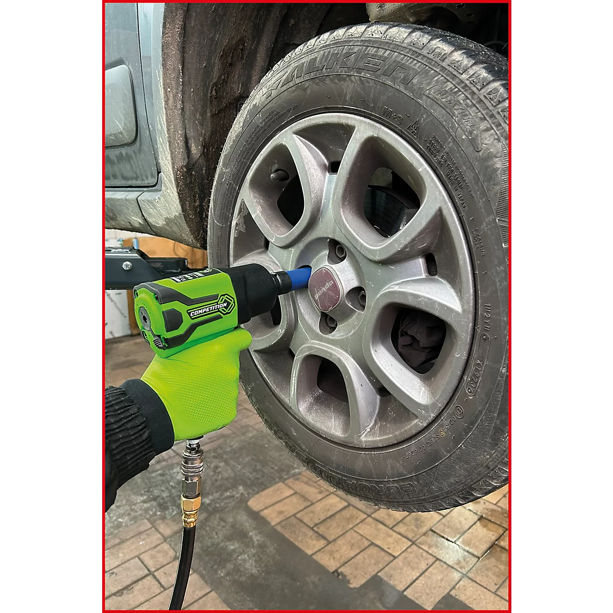 Hand mit neon-gelbem Handschuh nutzt grünen Druckluft-Schlagschrauber zum Lösen einer Radschraube am Autoreifen.