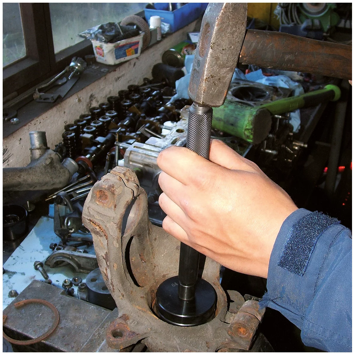 Hand nutzt Hammer und Dorn, um ein Lager in ein gebrauchtes Autoteil zu schlagen.