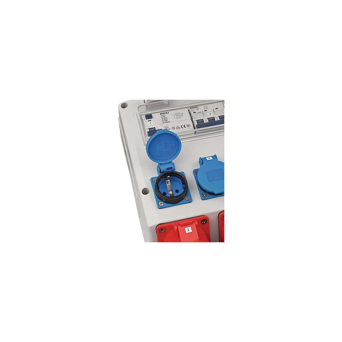Open blau stopcontact in een witte behuizing, daarnaast andere stopcontacten in rood en blauw. Boven zekeringkast.