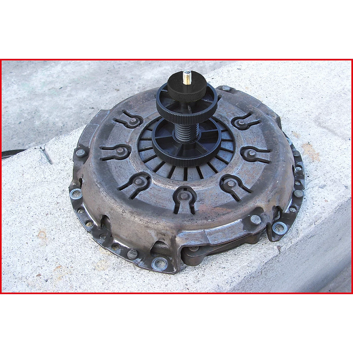 Ein verschmutzter Metall-Kupplungssatz mit einem schwarzen Führungsdorn liegt auf einem Betonblock.