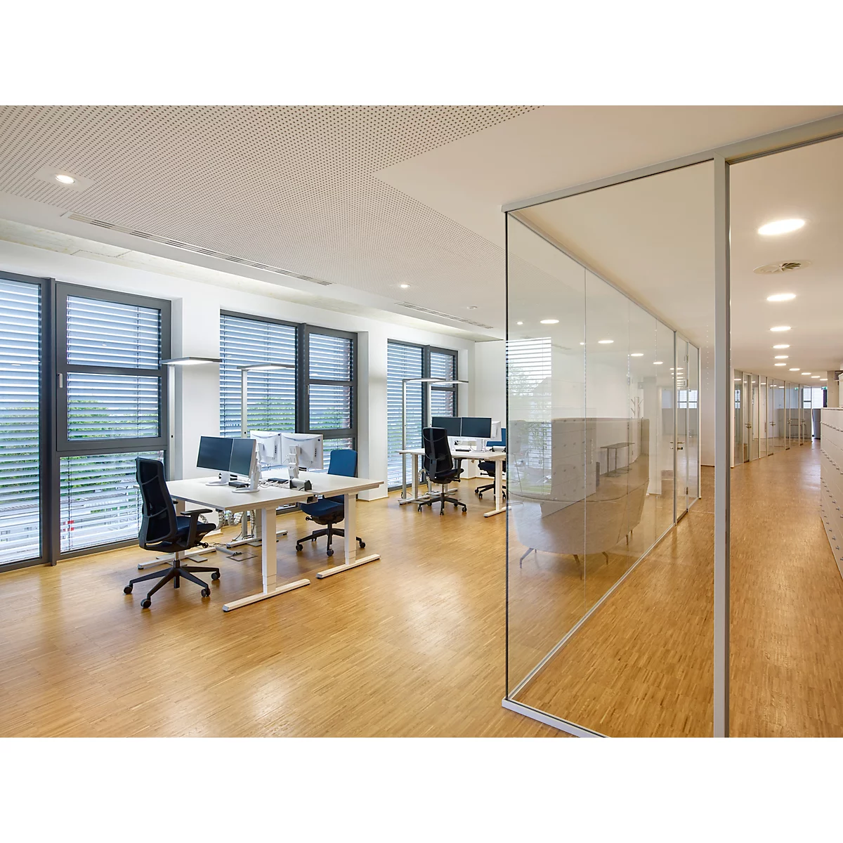 Bureau lumineux avec bureaux, chaises, fenêtres et parois vitrées. Plancher en bois et éclairage au plafond.