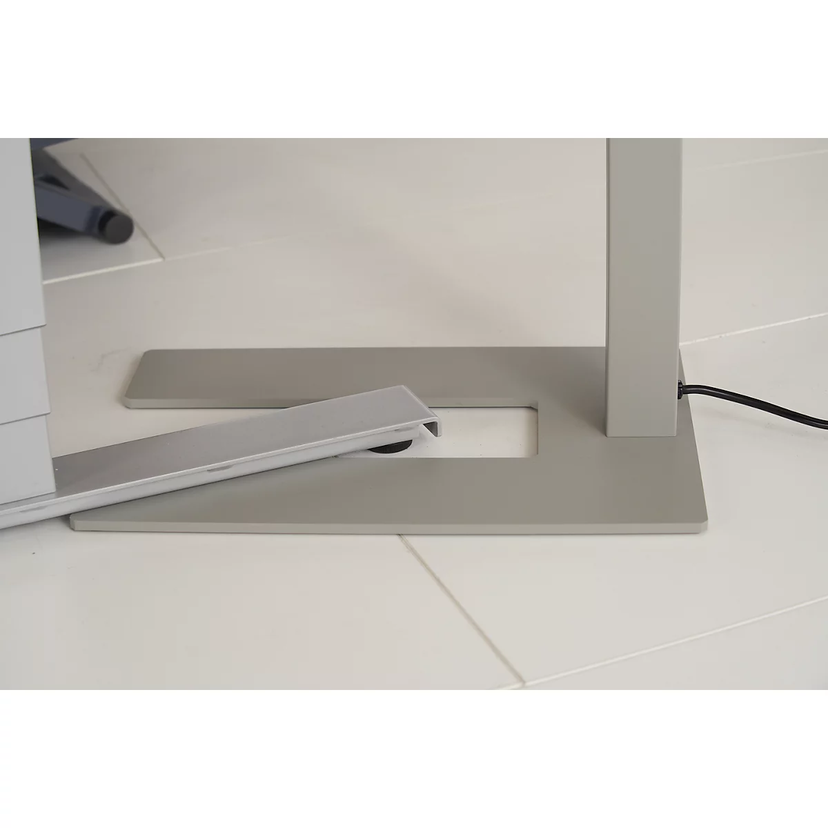 Base de lampe grise avec un renfoncement rectangulaire, câble et éléments argentés sur un sol blanc.