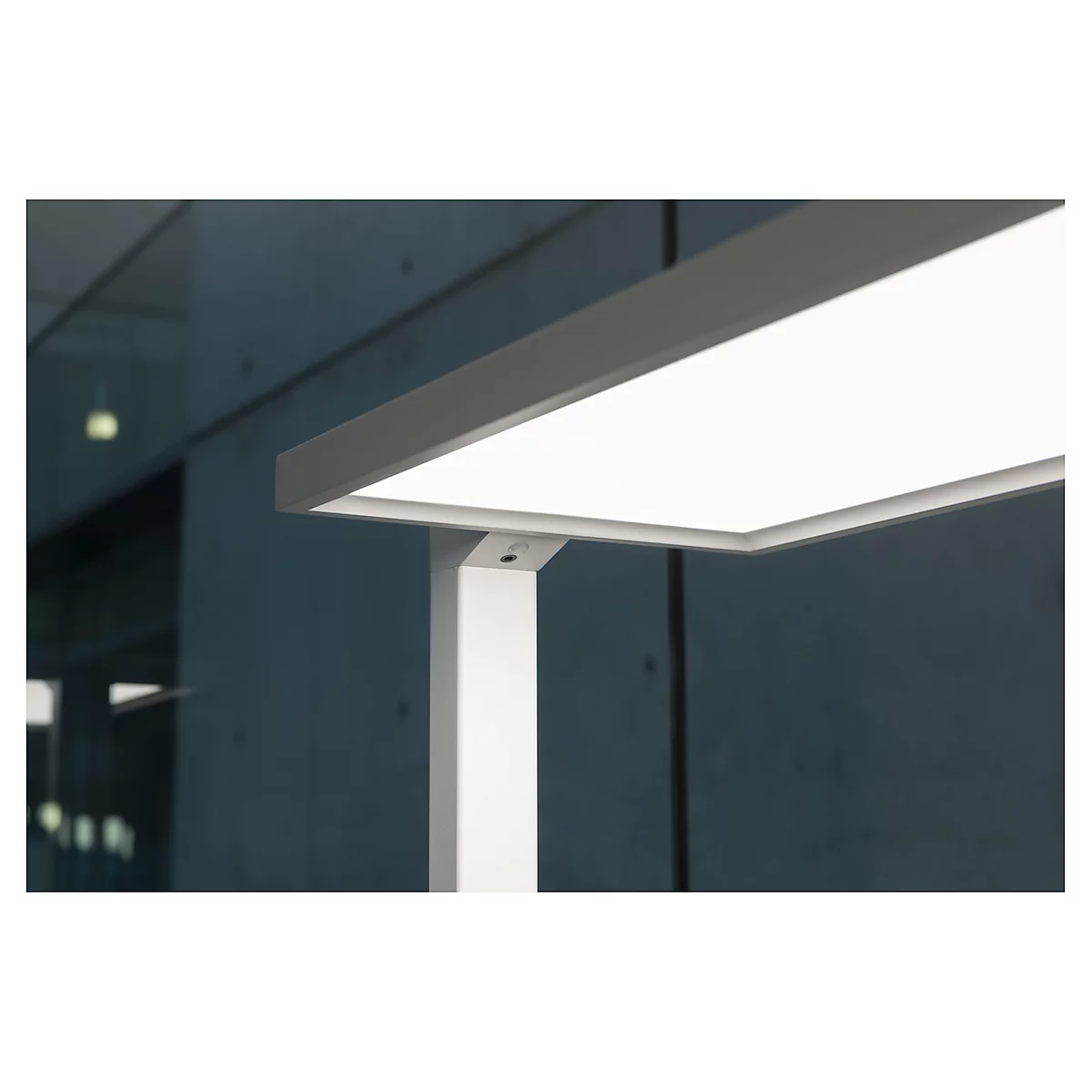 Gros plan d'une lampe de bureau LED blanche moderne avec un luminaire rectangulaire. L'arrière-plan est gris et flou.