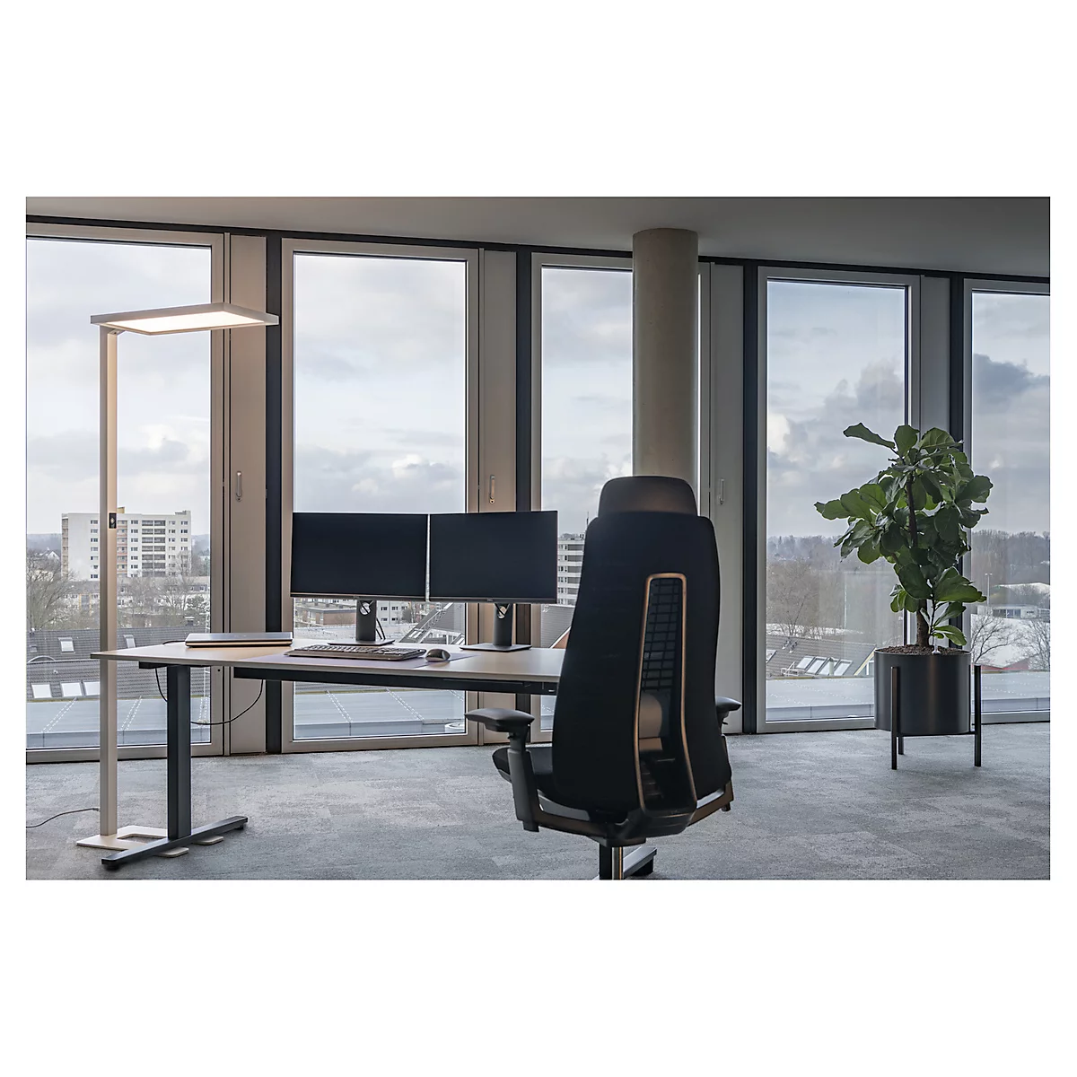 Un espace de travail moderne avec une lampe sur pied, un bureau et une chaise ergonomique devant une grande fenêtre avec vue sur la ville.