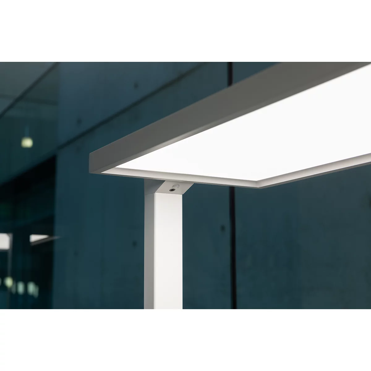 Gros plan d'une lampe de bureau moderne et brillamment éclairée. Le corps lumineux est rectangulaire et blanc, le cadre est blanc et anguleux.