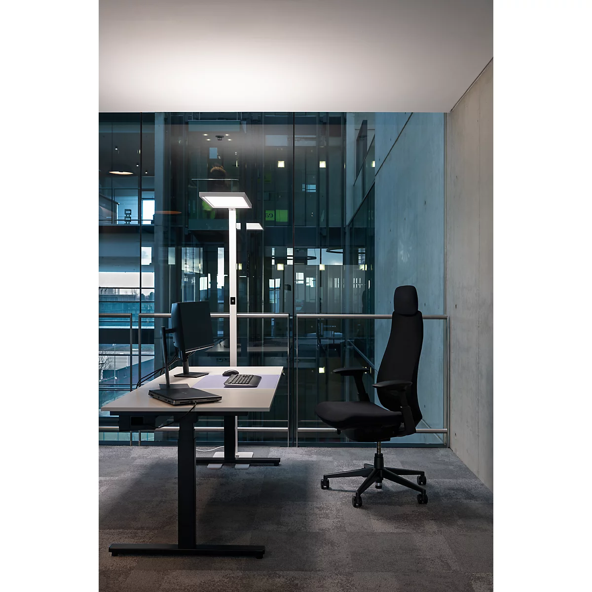 Un bureau moderne avec un bureau, une chaise de bureau, une lampe et une vue à travers une façade en verre.