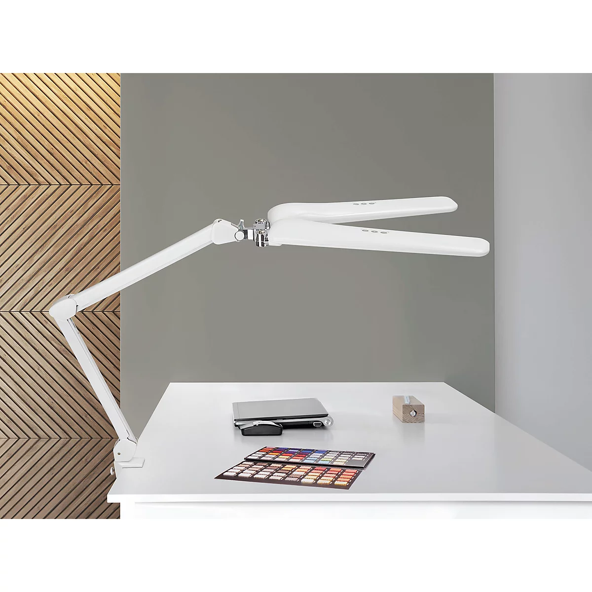 Lampe de bureau blanche au-dessus d'une table. Sur la table se trouvent un ordinateur portable, des échantillons de couleurs et un morceau de bois.