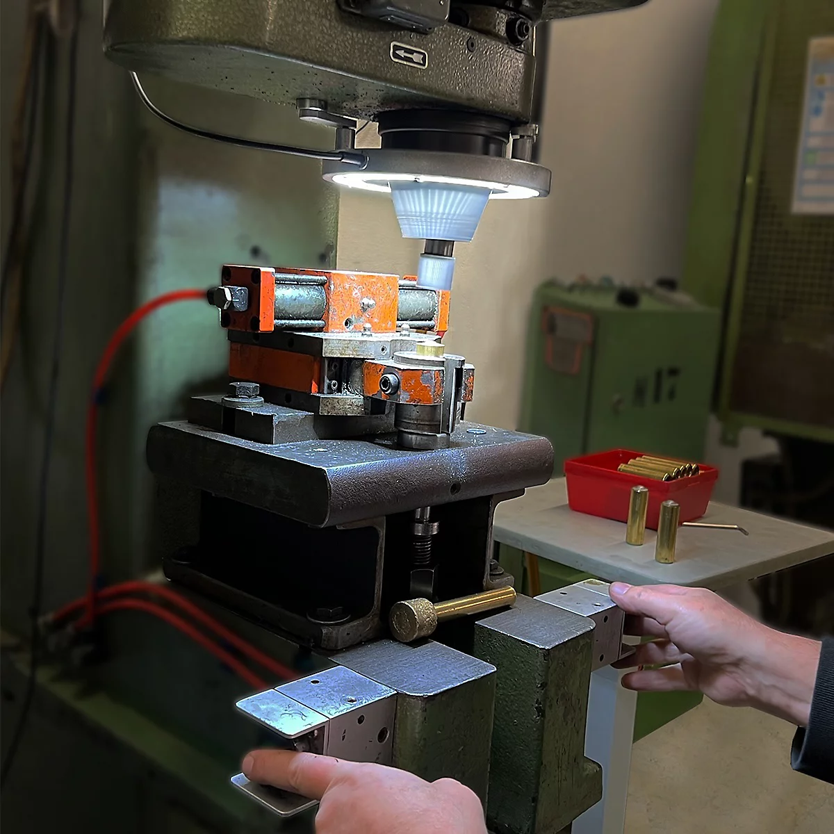 Usinage du métal. Machine en atelier, avec éclairage. Les mains actionnent la machine, à côté des pièces.