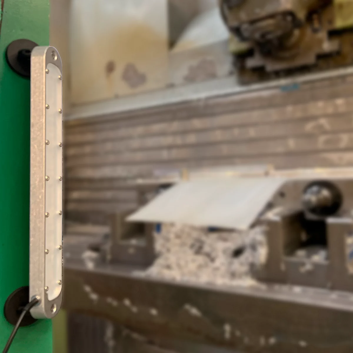Lumière LED allongée fixée à une machine verte. Une autre partie de la machine en arrière-plan.