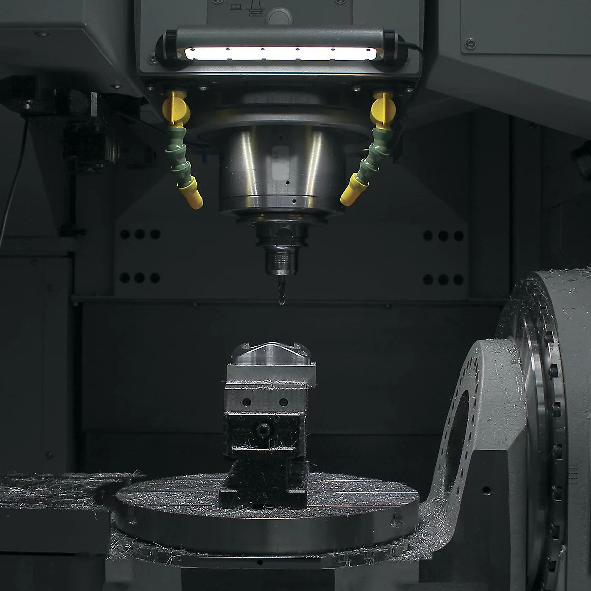 Machine-outil en cours d'utilisation : fraisage d'une pièce métallique, liquide de refroidissement, éclairage.