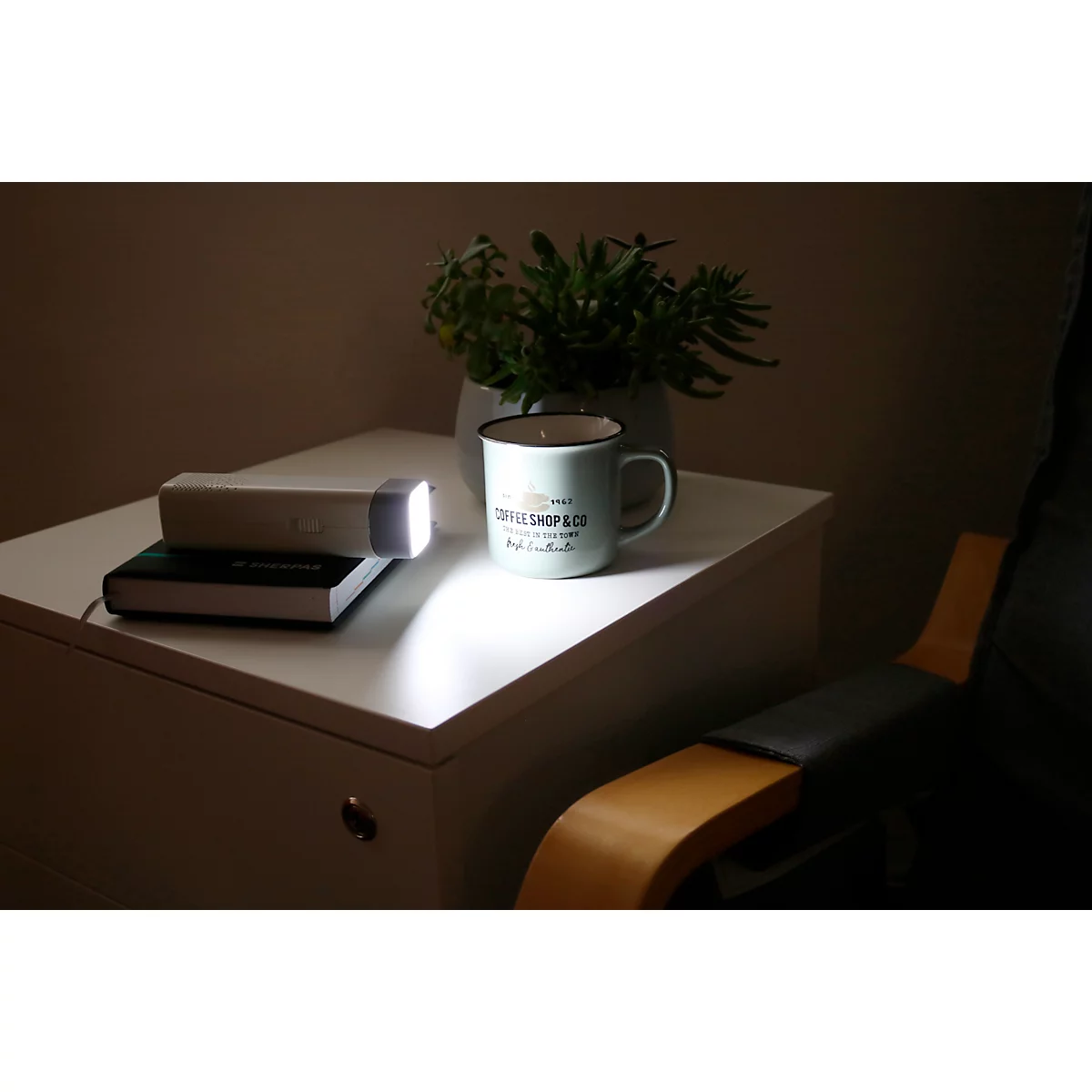 Une table de chevet blanche avec lampe, livre, tasse et plante. Un cône de lumière illumine la scène.