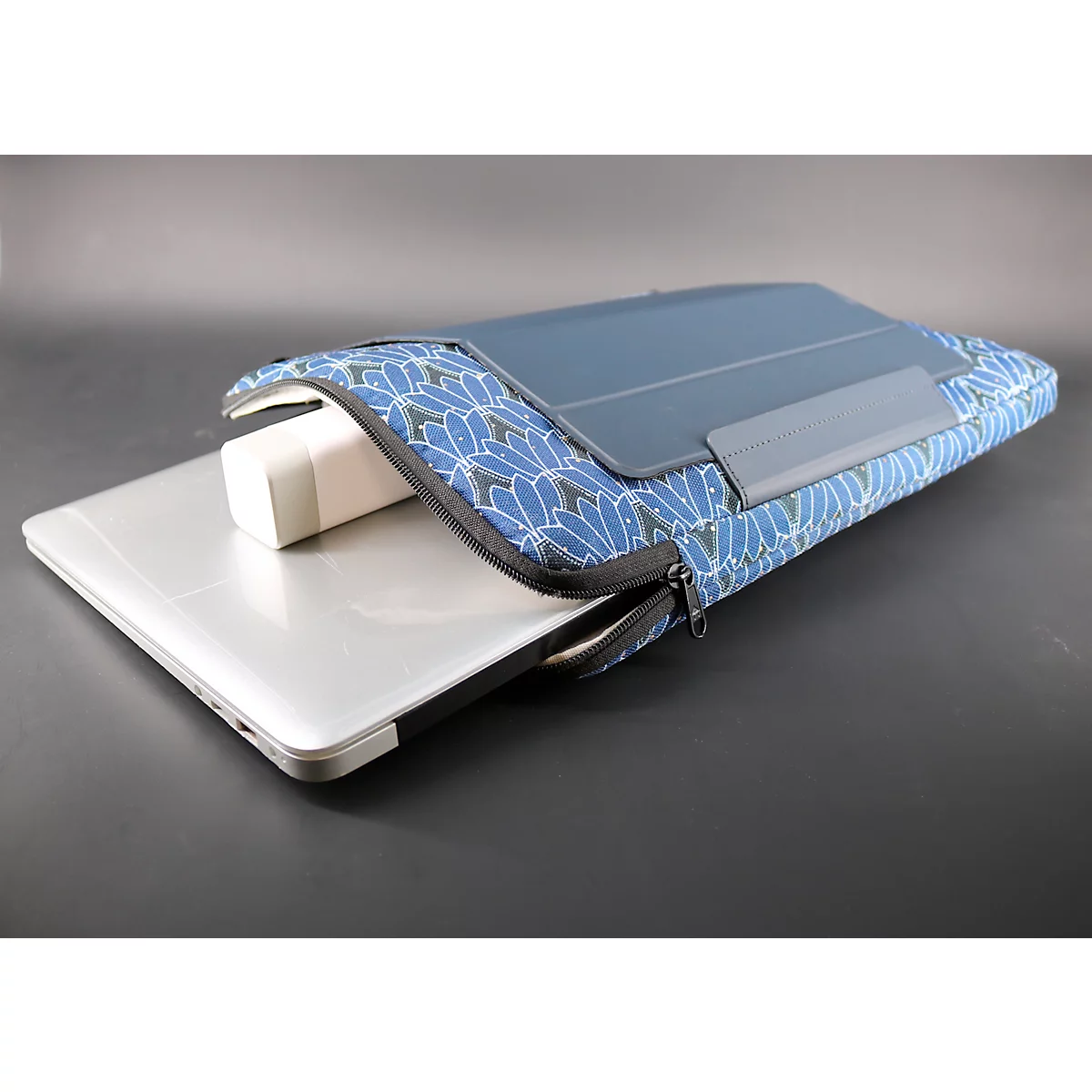Housse d'ordinateur portable avec fermeture éclair, ordinateur portable et adaptateur secteur. L'étui est bleu avec des motifs floraux blancs.