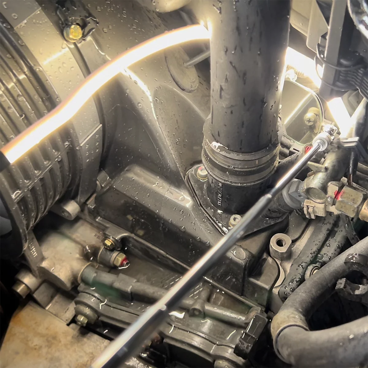 Gros plan sur un compartiment moteur avec des tuyaux, des conduites et des composants métalliques. Une lumière vive illumine la scène.