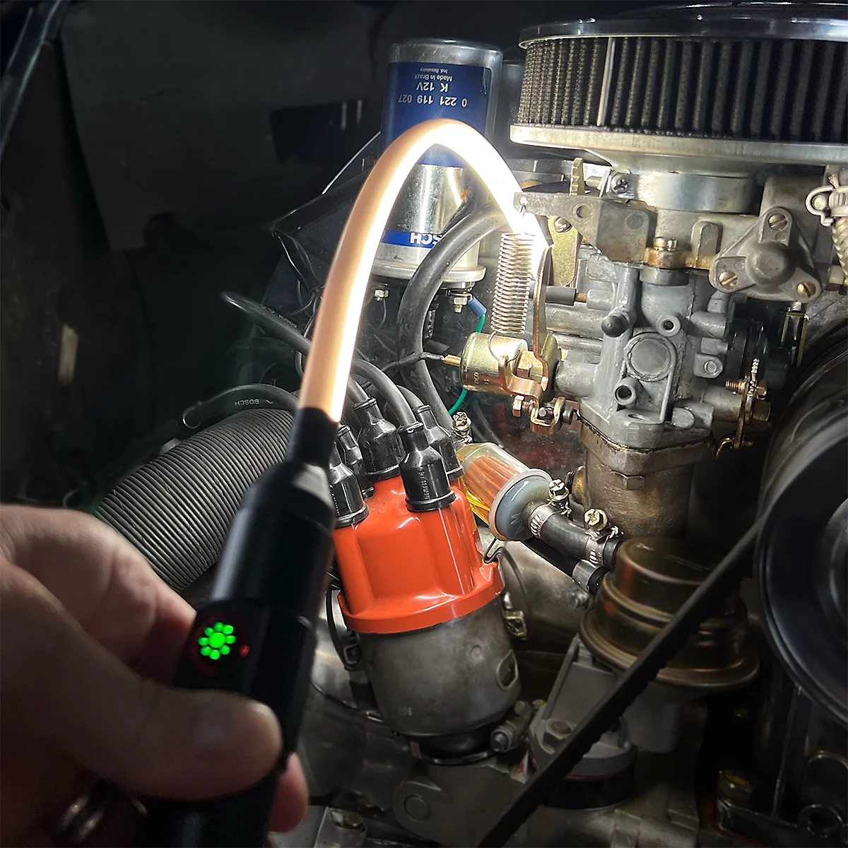 Main tenant une lampe d'inspection flexible sur le moteur d'une voiture ancienne.