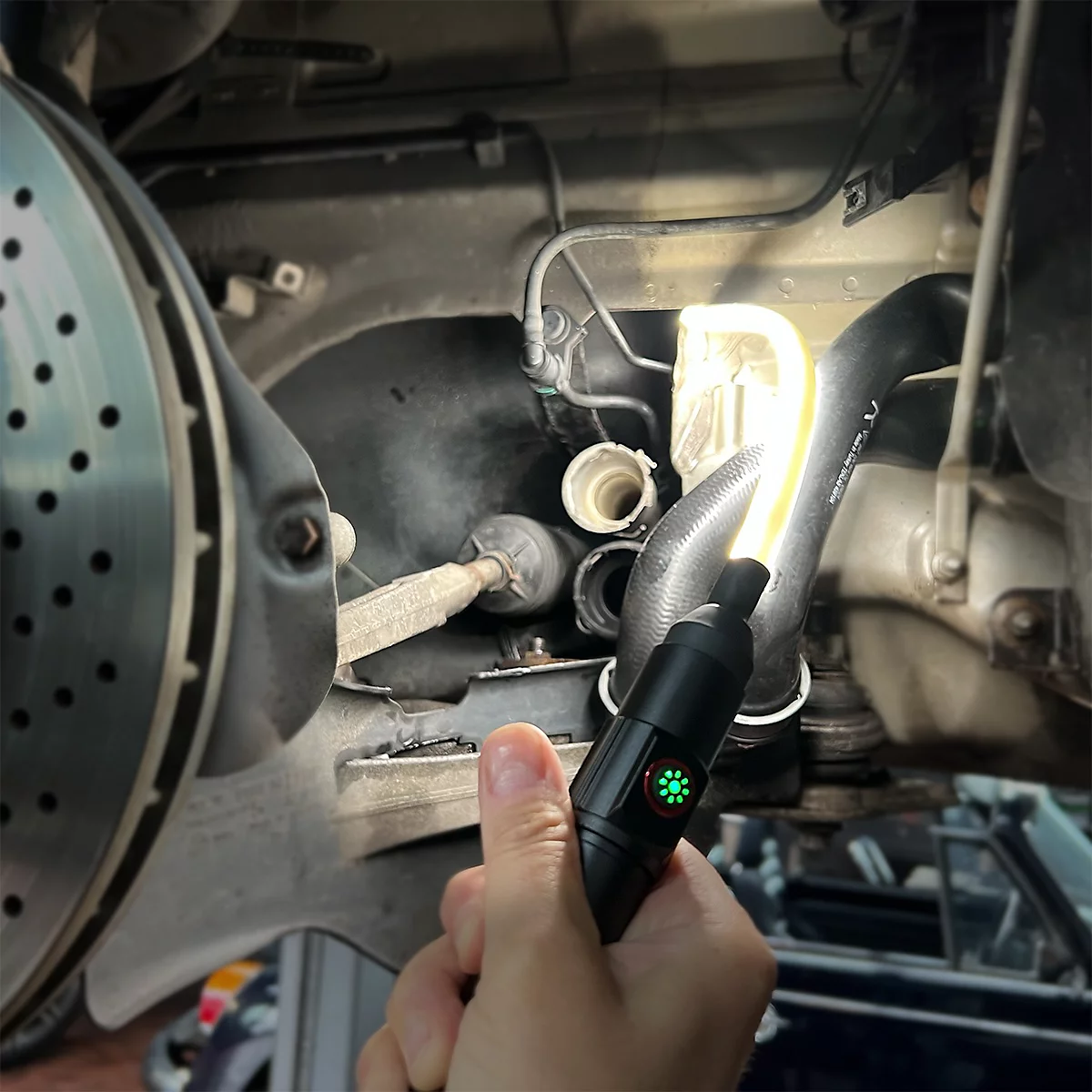 Une main tient une lampe de poche LED noire, éclairant le compartiment moteur d'une voiture. La lumière verte est allumée.