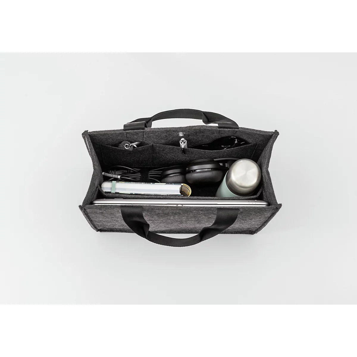 Grijze vilten organizer gevuld met laptop, koptelefoon, waterfles en accessoires, tegen een witte achtergrond.