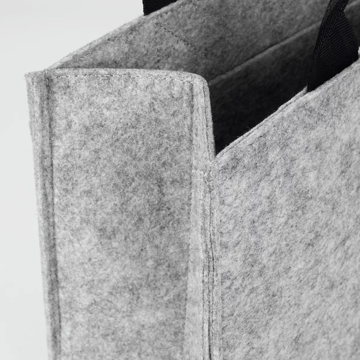 Close-up van een grijze vilten tas met zwarte handgreep, met textuur en naden.