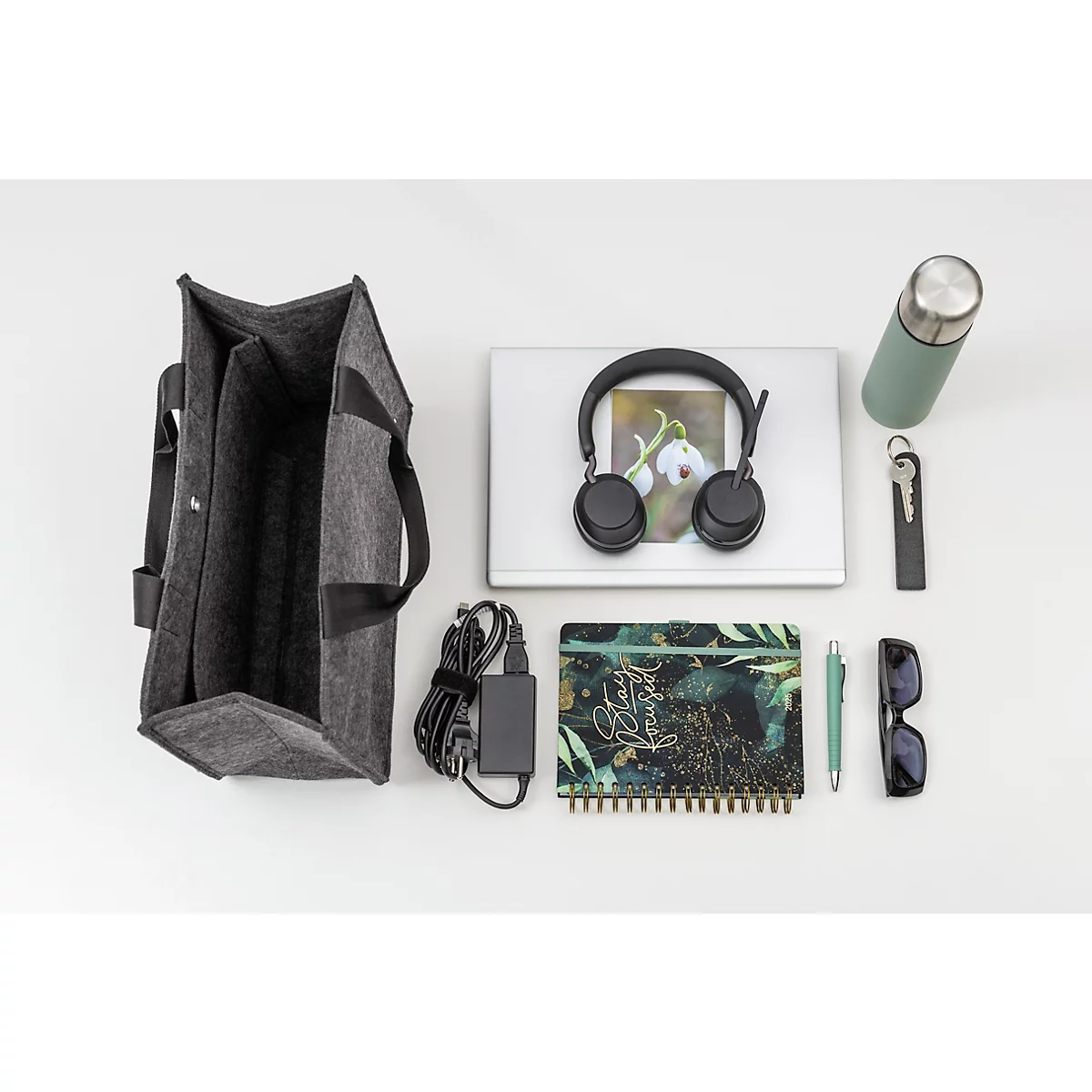 Graue Filztasche, Laptop, Kopfhörer, Notizbuch, Sonnenbrille und Trinkflasche auf weissem Grund.