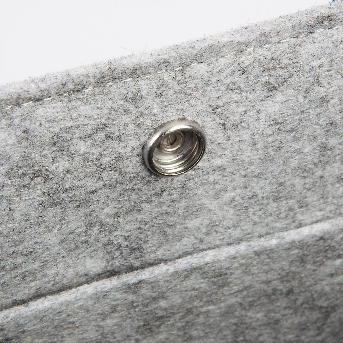 Detailaufnahme eines grauen Filzmaterials mit einem silbernen Druckknopf.