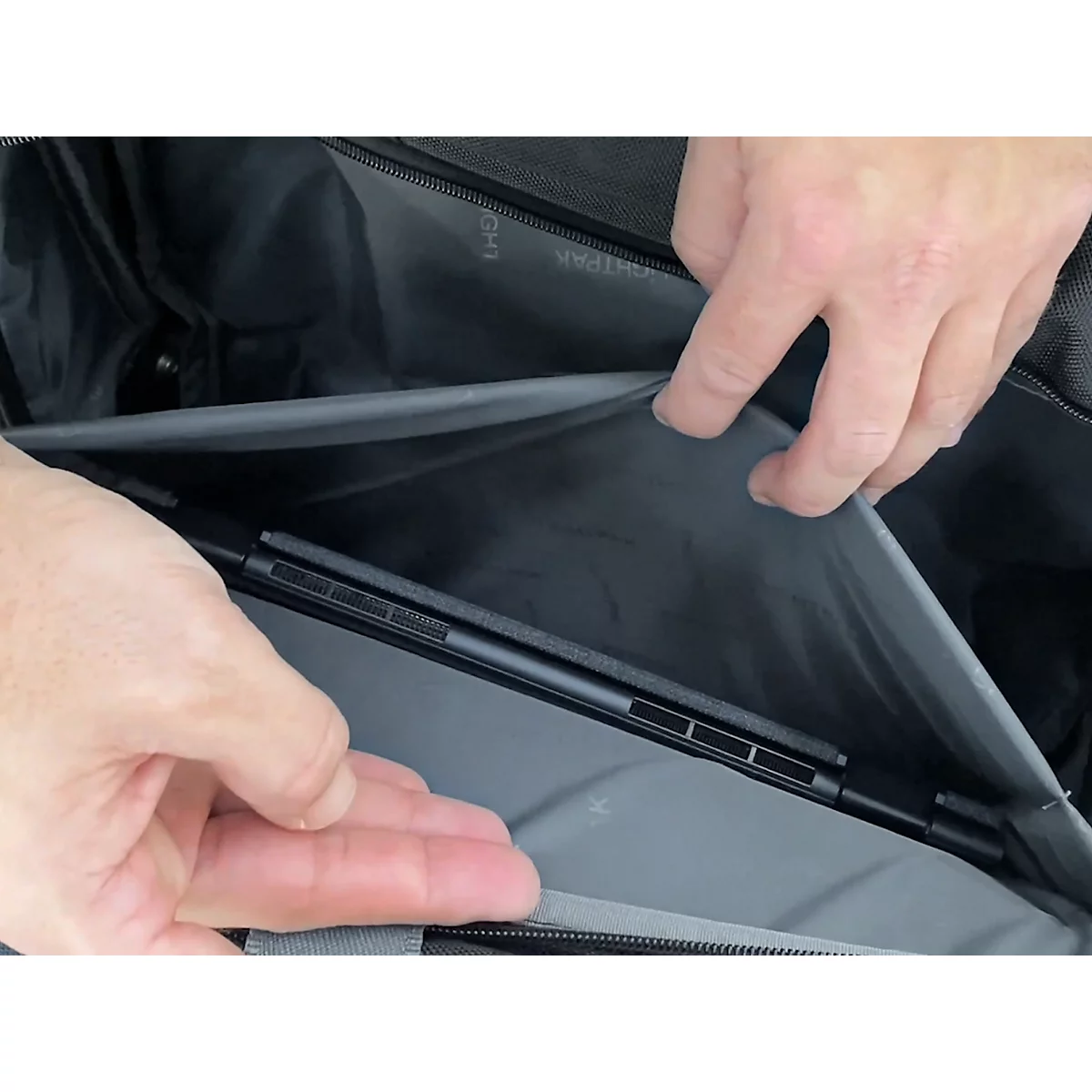 Hände öffnen eine Tasche, die ein Laptop enthält. Der Laptop liegt in einer grauen Tasche.