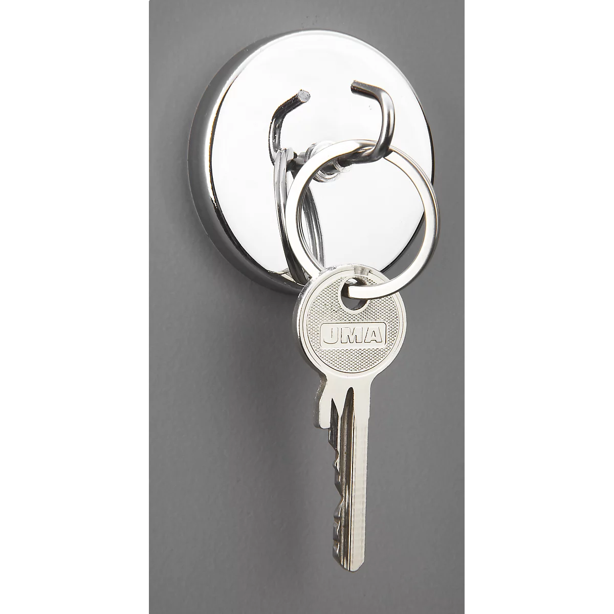 A keychain with a door key hangs from a round, silver-colored magnet on a gray background.