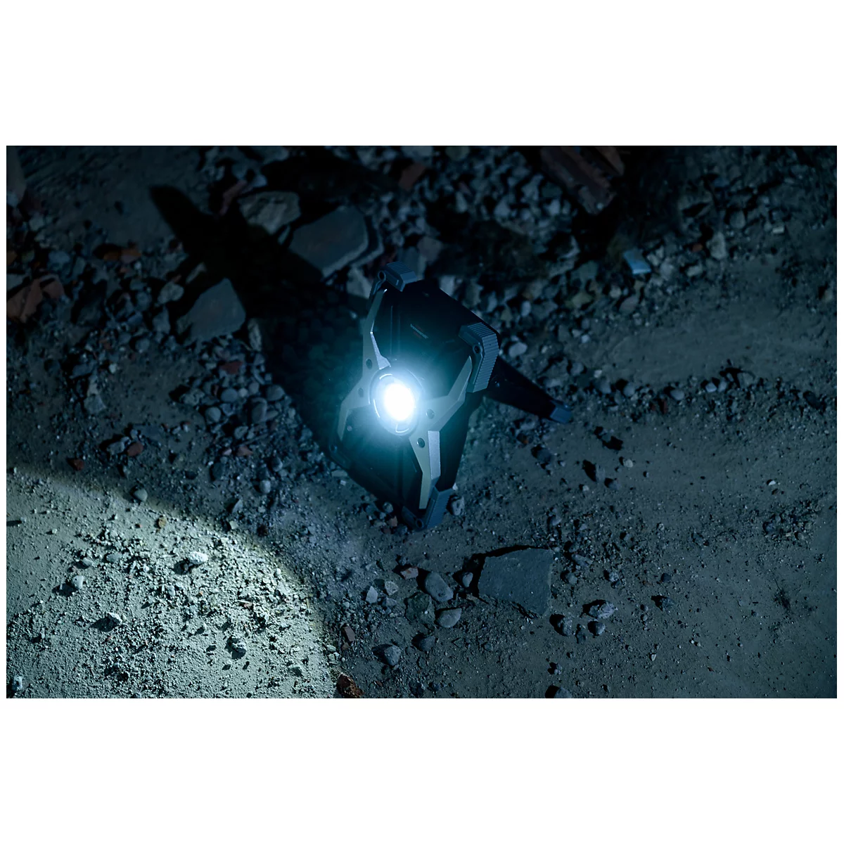 Eine Taschenlampe leuchtet auf den Boden und wirft einen Schatten auf die Steinfläche, umgeben von Schutt.