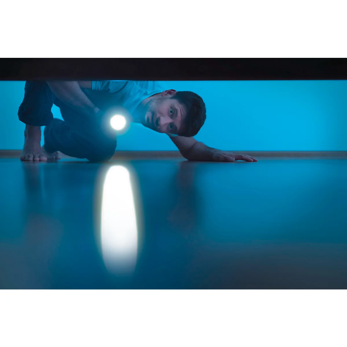 Man shining flashlight under furniture, searching for something.