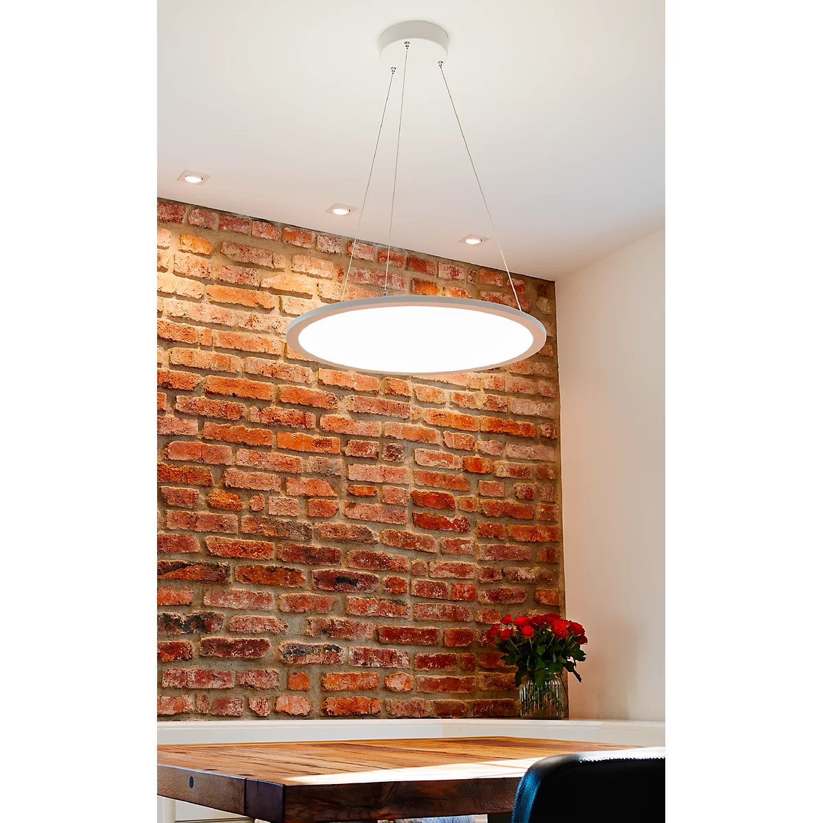 Pendant lamp over a wooden table. Behind it a brick wall and a bouquet of roses.