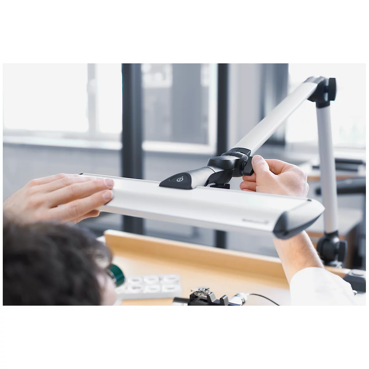 Person adjusting a desk lamp. The lamp has a long, rectangular light source connected to an articulated arm.