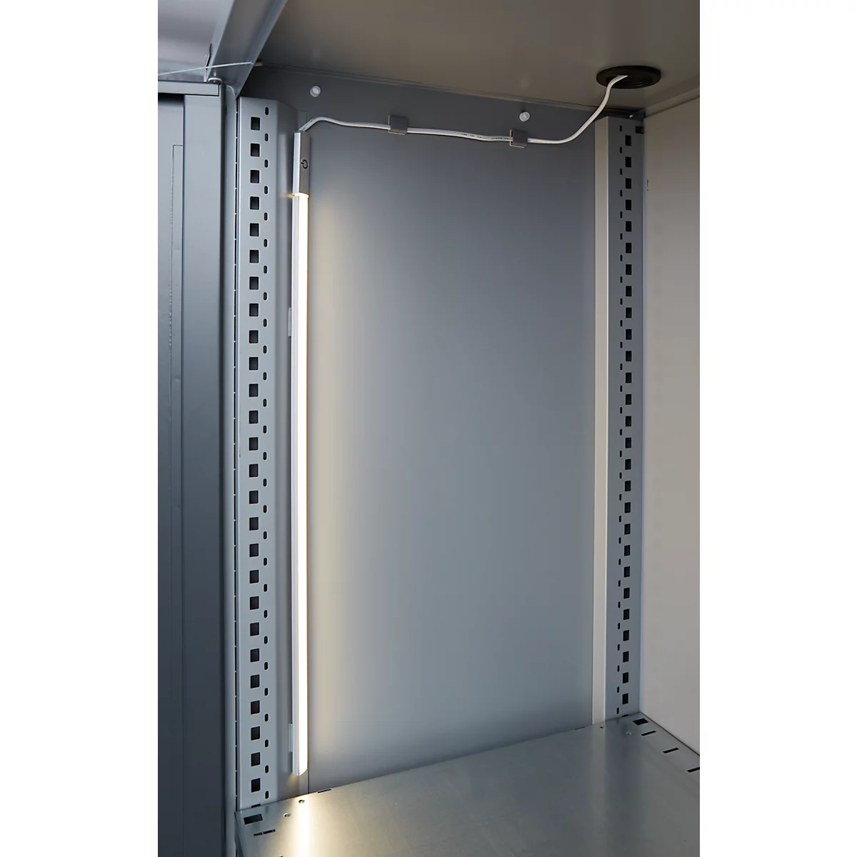 Inside view of a cabinet with LED light. Gray metal walls and frames. A white cable leads to the ceiling.