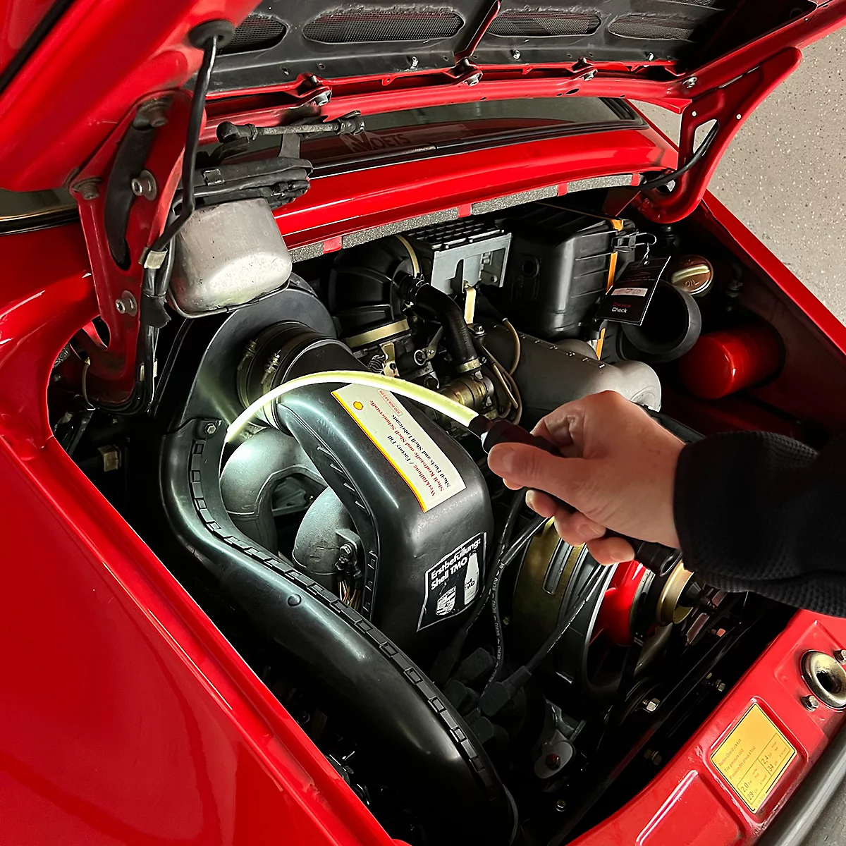 Ein offener Motorraum eines roten Oldtimer-Autos. Eine Hand hält eine Taschenlampe, um in den Motor zu leuchten.