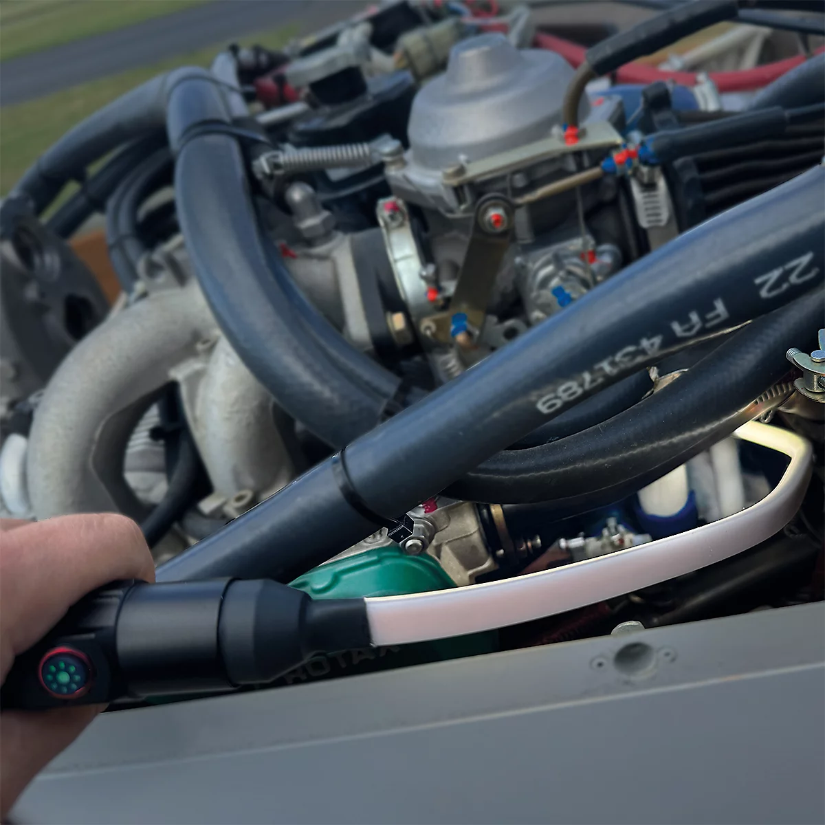 Ein Mann hält eine Lampe, die einen Motorraum ausleuchtet. Schwarzer Griff, weißes Licht. Im Hintergrund: Rohre und Motorteile.