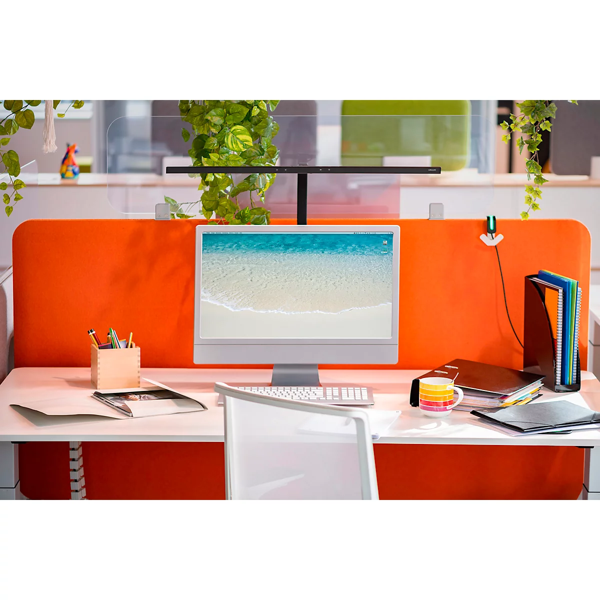 Werkplek met bureau, computerscherm, planten en kantoorbenodigdheden. Heldere en vriendelijke werkomgeving.