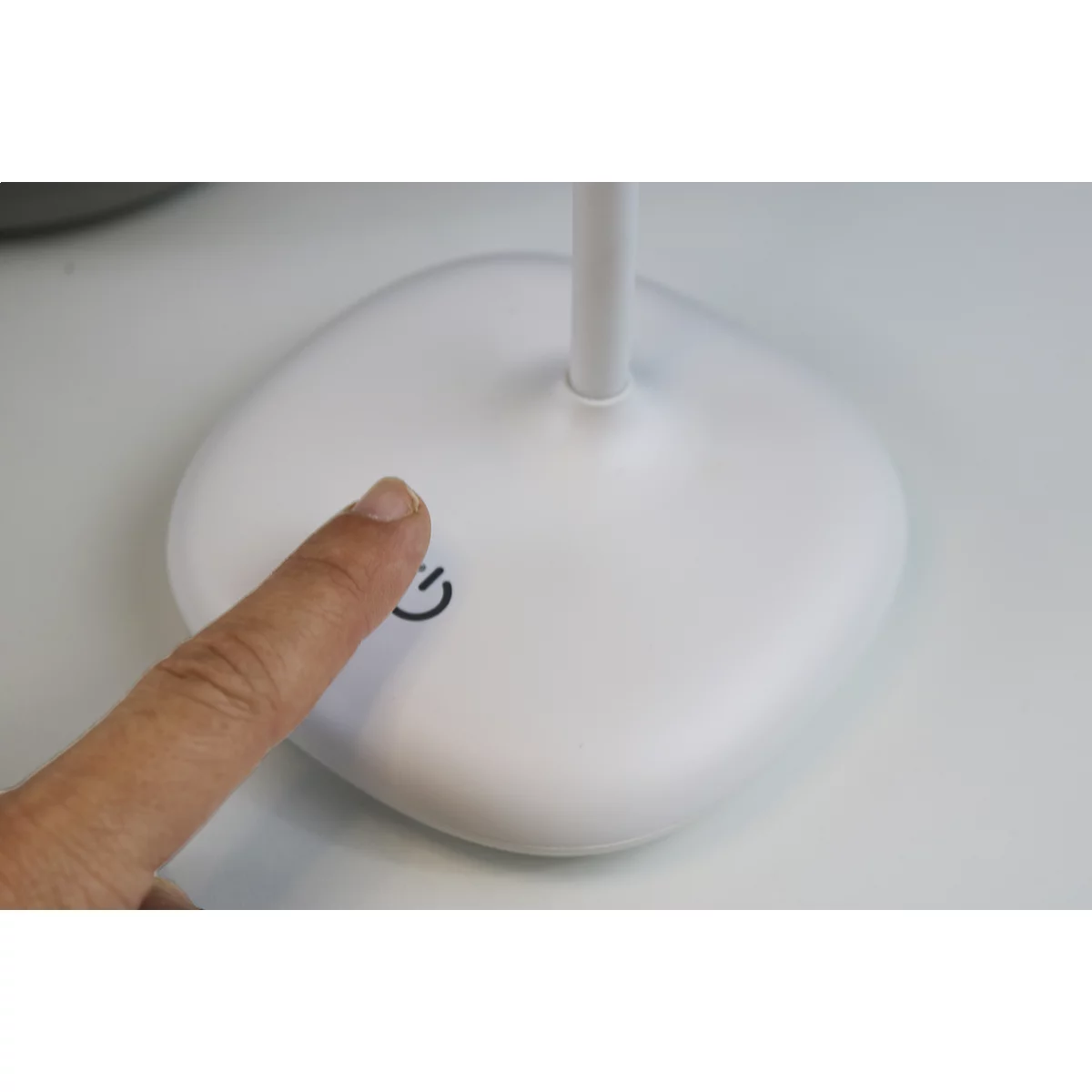 Ein Finger berührt den Ein- und Ausschalter einer weißen Schreibtischlampe.