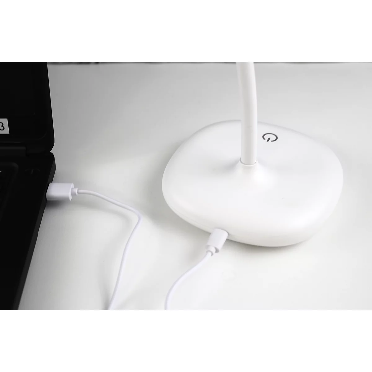 Eine weiße Schreibtischlampe mit USB-Anschluss, der mit einem Laptop verbunden ist. Auf dem Lampenfuß ist ein Ein-/Aus-Symbol.