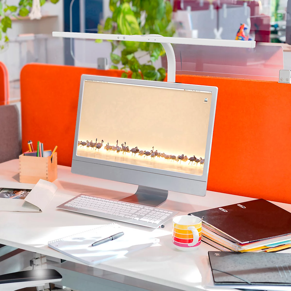 Arbeitsplatz mit Computer, Tastatur, Stiften und Papieren, mit Flamingo-Hintergrund. Orange Trennwände.