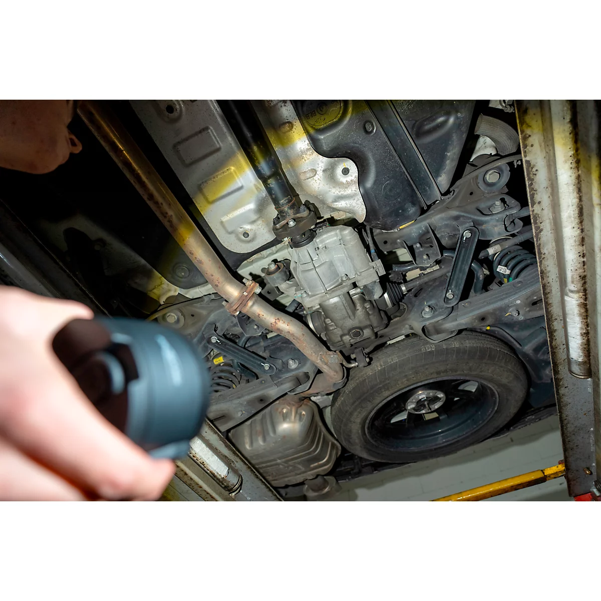 View from under a car. The underbody is visible, a person is holding a lamp.