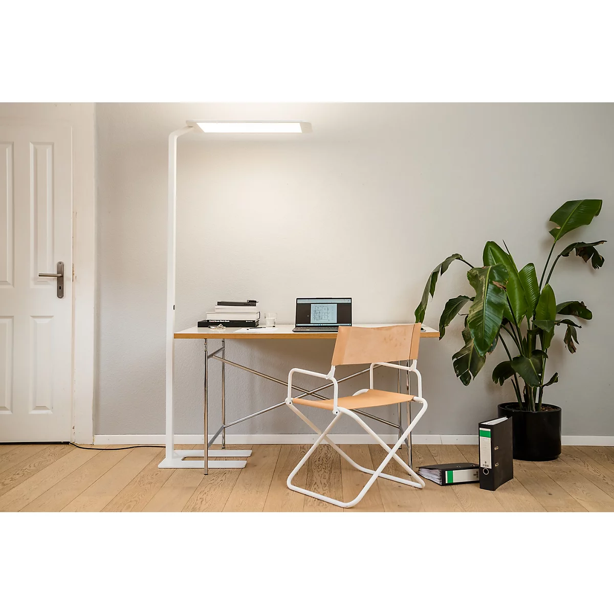 Heller Arbeitsplatz mit Lampe, Schreibtisch, Laptop, Stuhl und Pflanze.