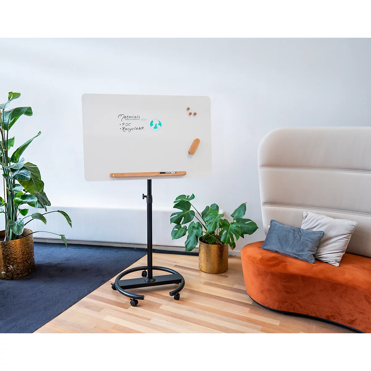 Tableau blanc sur un pied noir avec stylo et plantes dans un bureau. Une chaise est à l'arrière-plan.