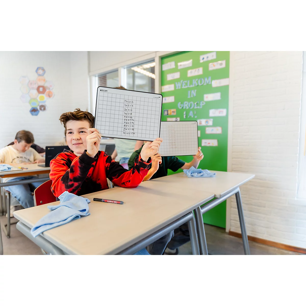 Ein Junge in einem Klassenzimmer hält ein beschriebenes Whiteboard in die Höhe.