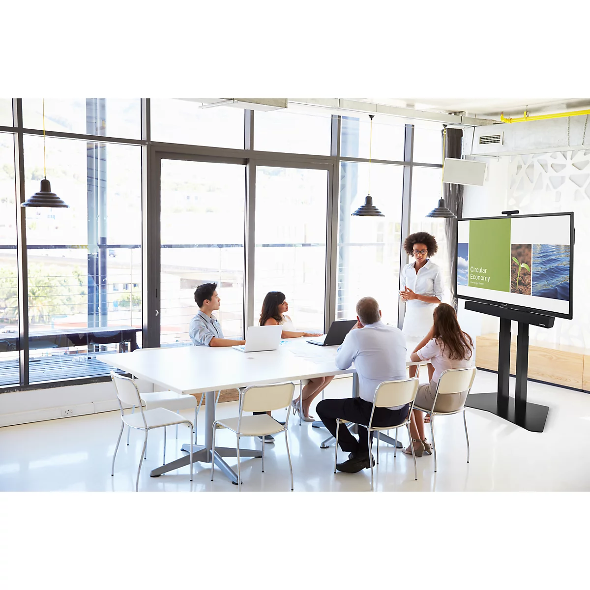 Un groupe de collègues dans une salle de conférence lumineuse suivant une présentation sur grand écran.
