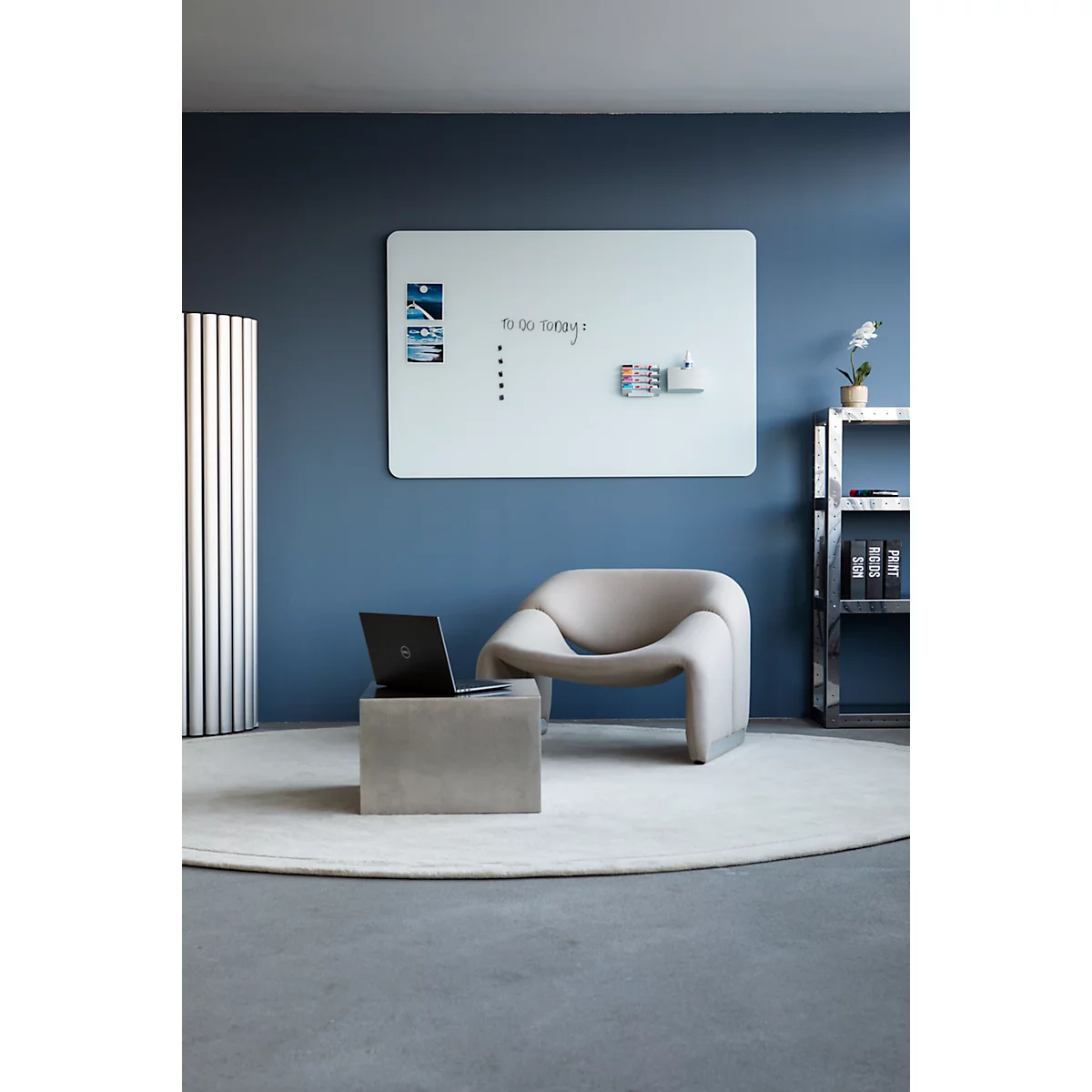 Un bureau moderne avec des meubles et des accessoires design. Un tableau mémo, une chaise, une table basse et un ordinateur portable sont visibles.