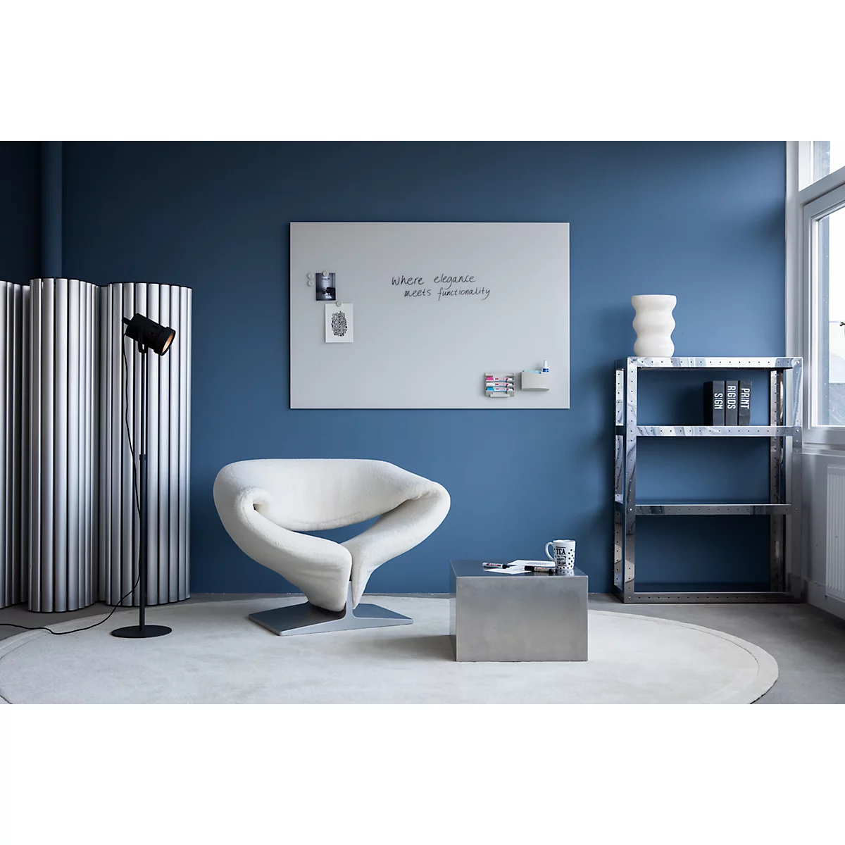 Un bureau moderne avec tapis beige, chaise blanche, fond bleu, bureau, table d'appoint, tableau blanc et étagère.