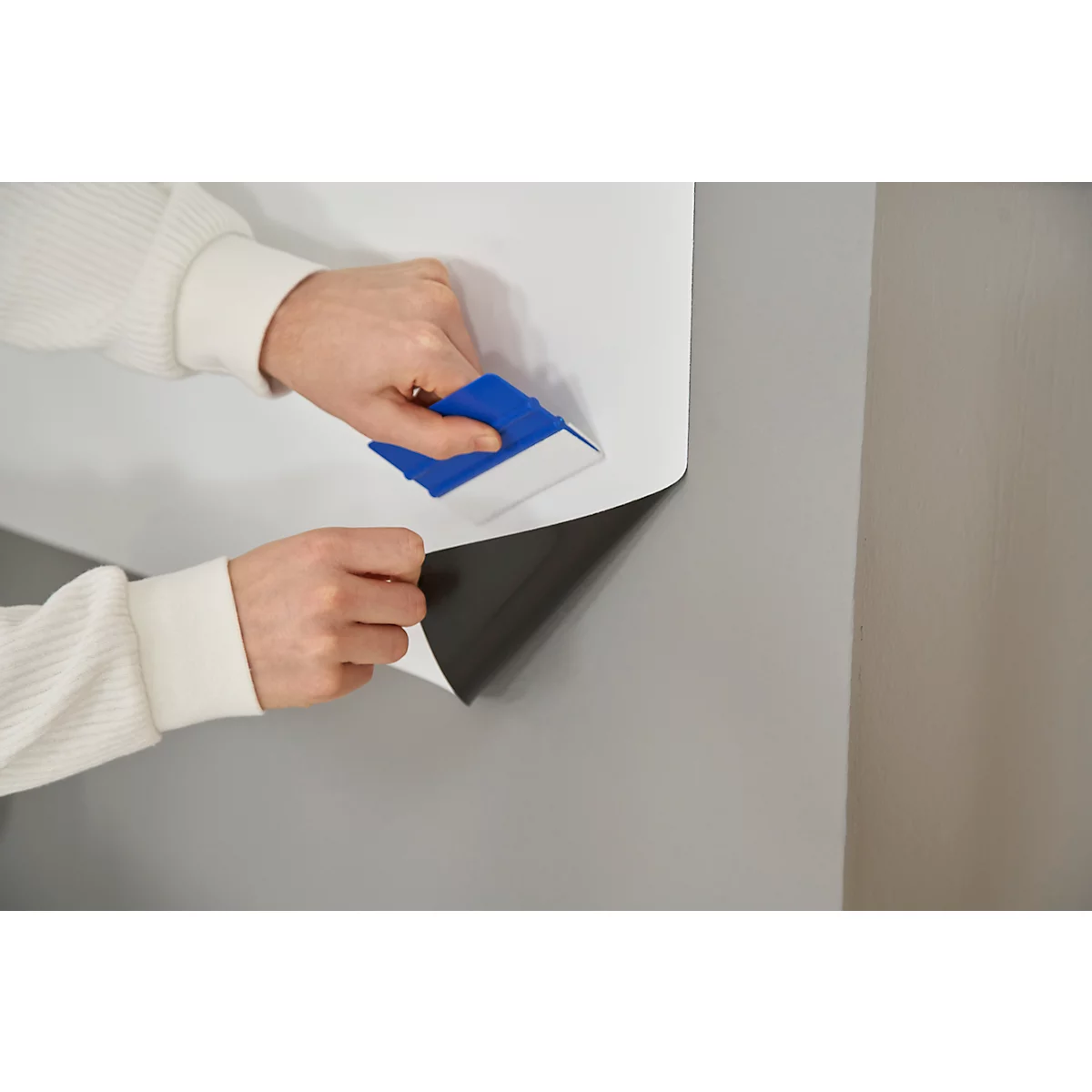 A person applying self-adhesive film to a wall with a blue squeegee.