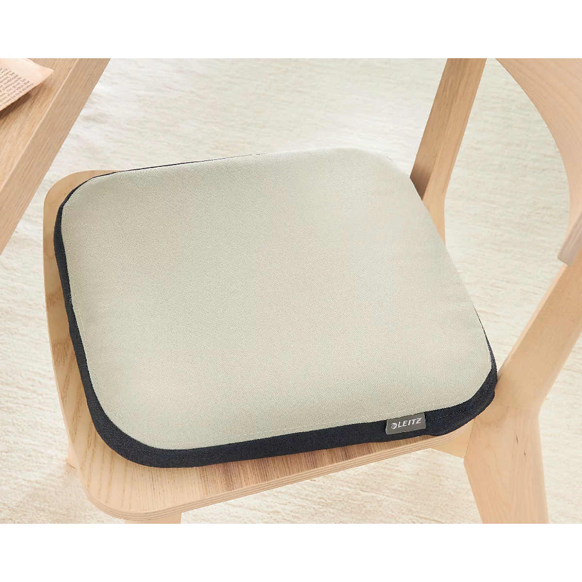 Ein quadratisches Sitzkissen in Beige mit dunkelblauer Umrandung auf einem Holzstuhl. Zertifizierungen und Auszeichnungen.