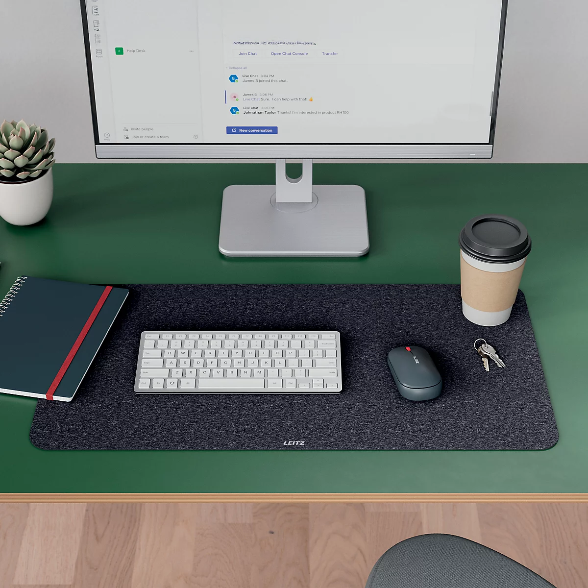 Bureau met monitor, toetsenbord, muis, notitieboek, koffiekopje en plant. Alles is geplaatst op een grijze vilten mat.