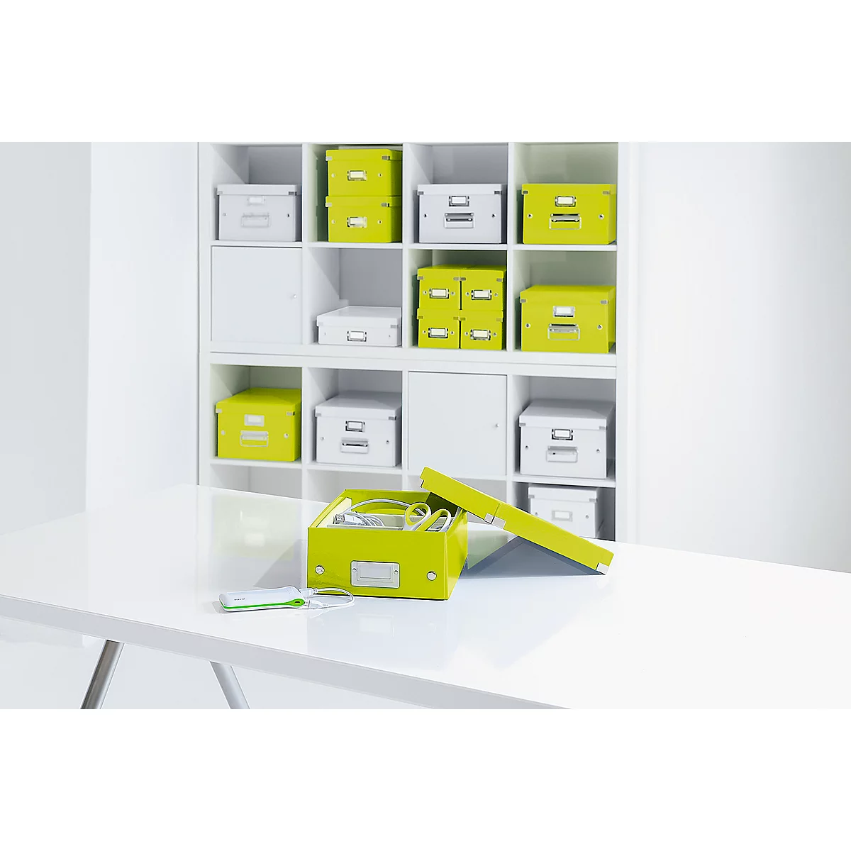 An open lime green box with cables and paper in front of a white shelf full of boxes.