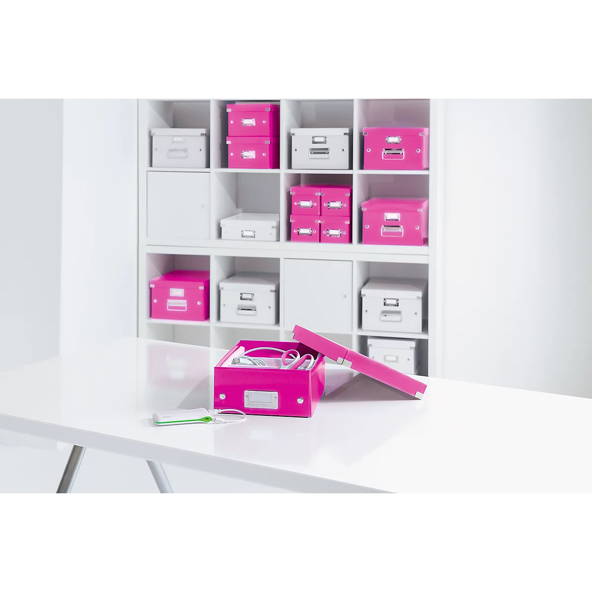 An open, pink storage box on a white table with other boxes in a white shelf.