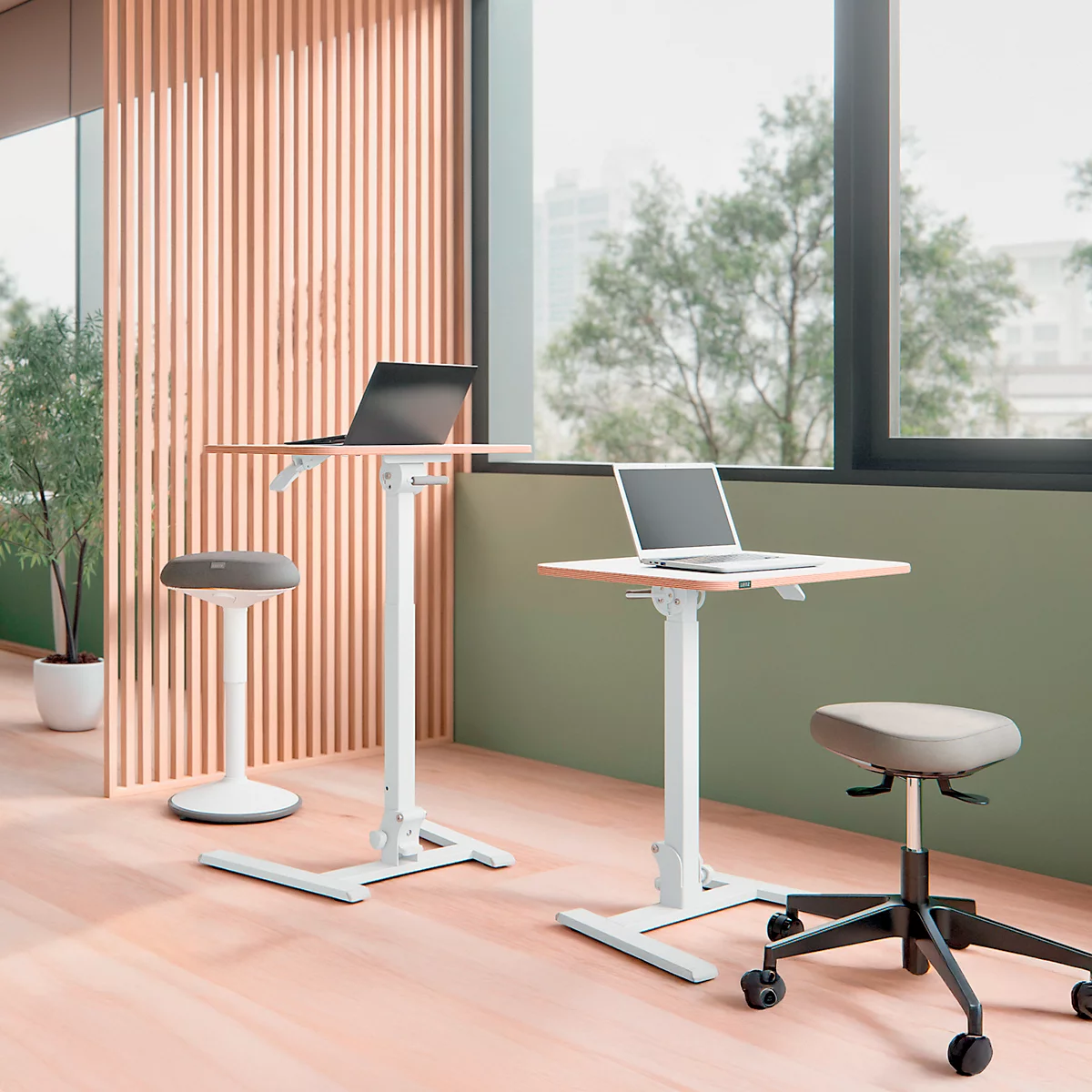 Kantoor met in hoogte verstelbare bureaus en stoelen; laptops staan op de tafels. Heldere inrichting, groot raamzicht.